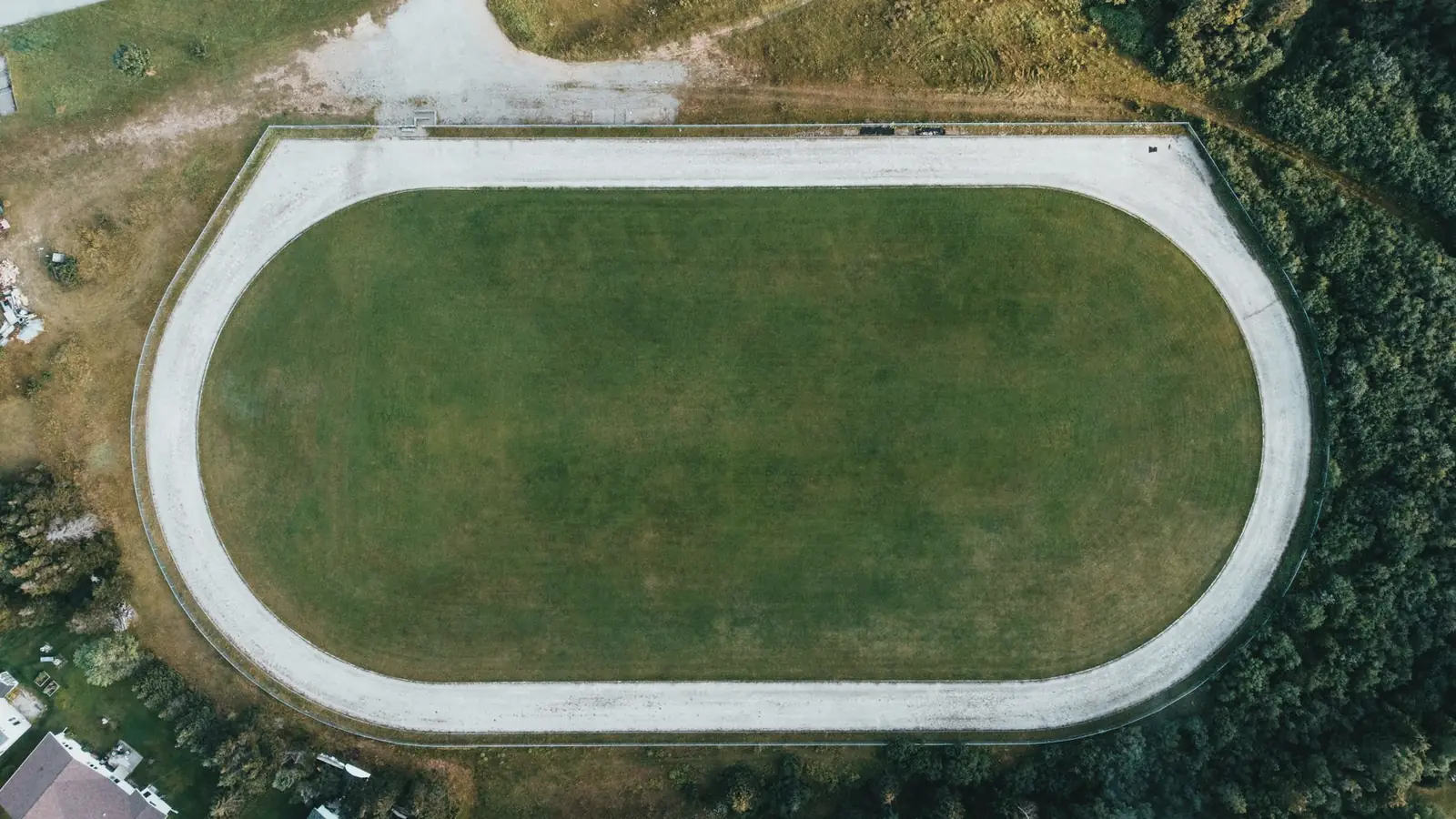 An open running track and field seen wide, ringed by hills